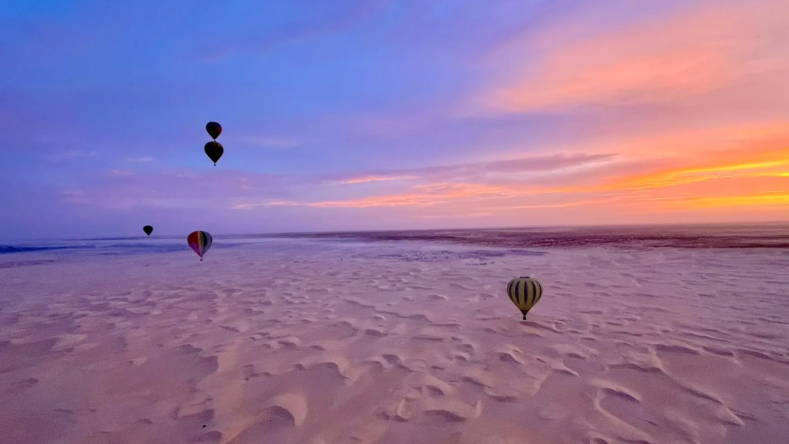 Balões de ar quente ao nascer do sol sobre dunas